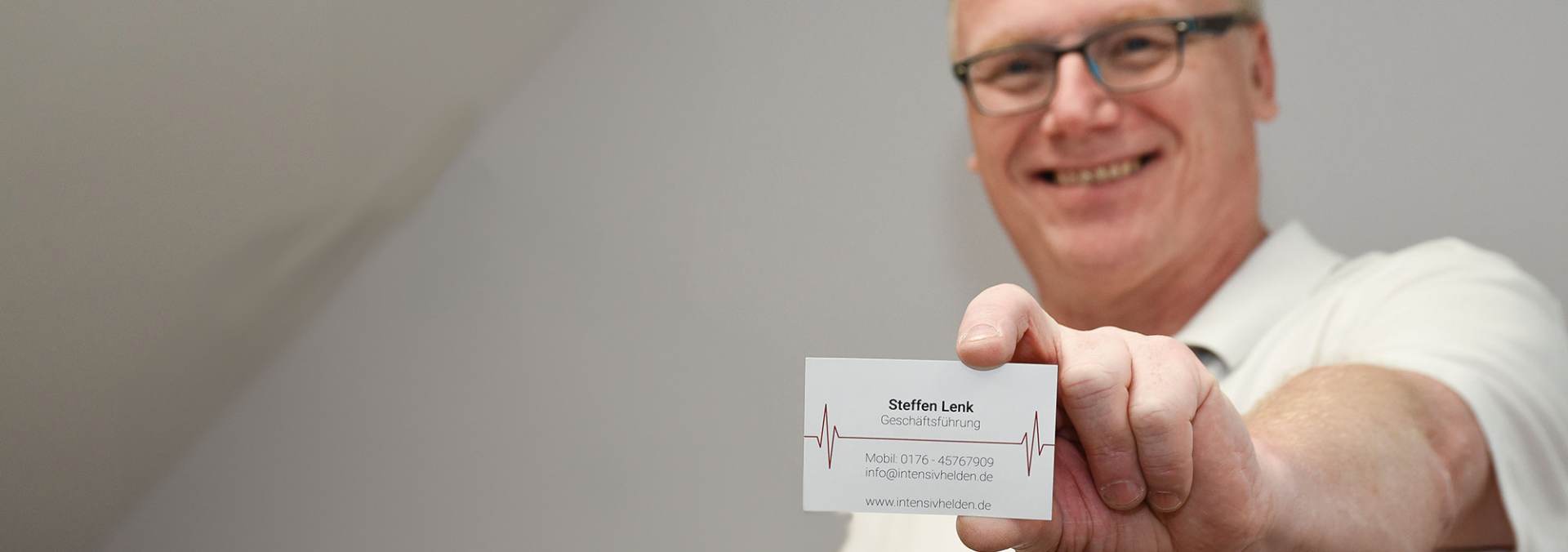 Herr Lenk hält lächelnd seine Visitenkarte ins Bild